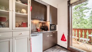 A compact kitchen with a microwave, stove, and dishwasher, a sliding glass door to a balcony with outdoor furniture. - Apartment 'Fleury' with Mountain View and Balcony (Mieussy)