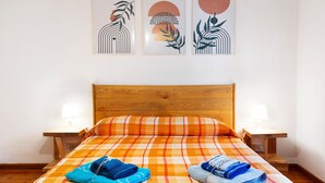 Ein Zimmer mit einem Bett, zwei Nachttischen und drei an der Wand hängenden Kunstwerken.