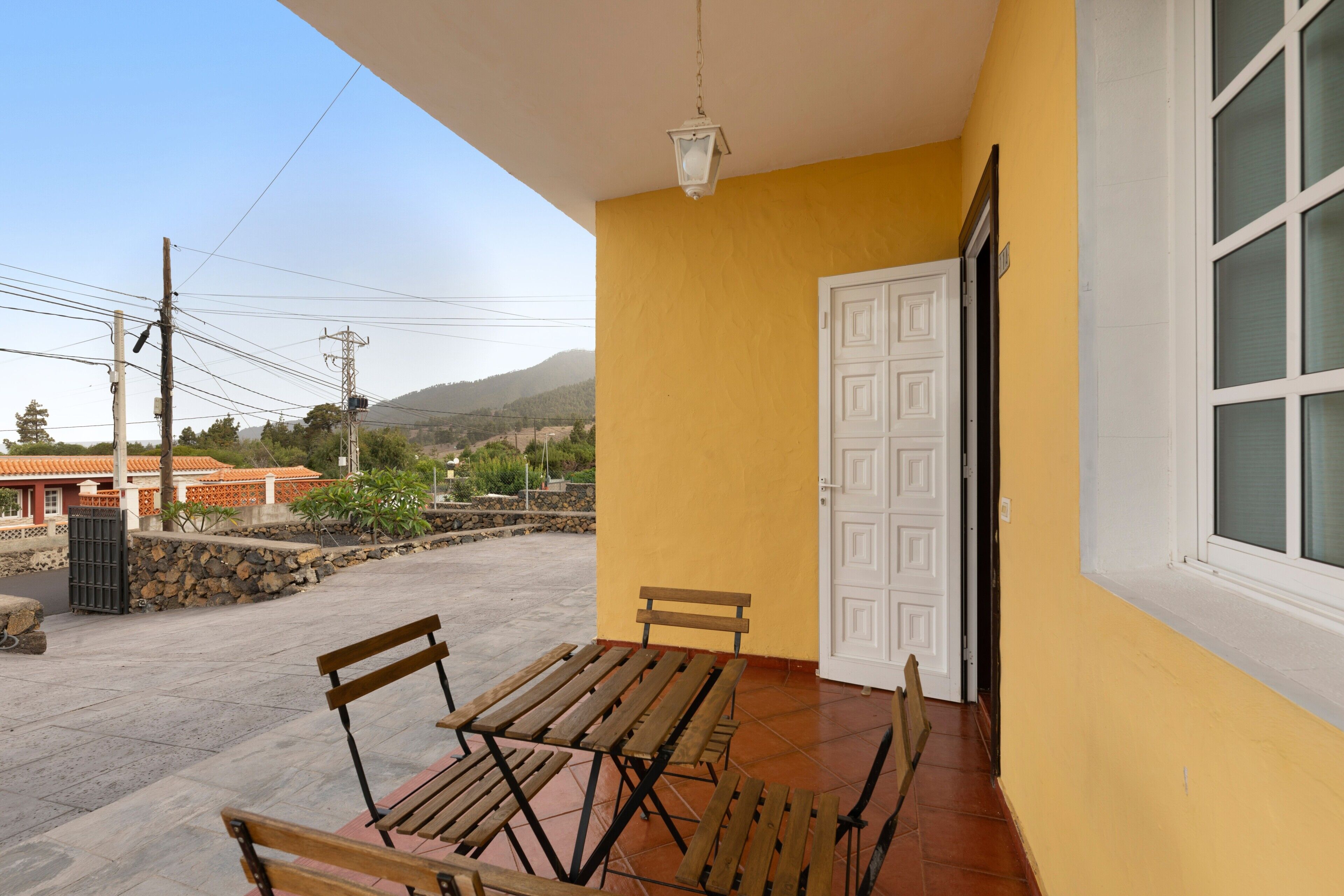 Un patio con una mesa, bancos, una puerta blanca y vistas del paisaje circundante.
