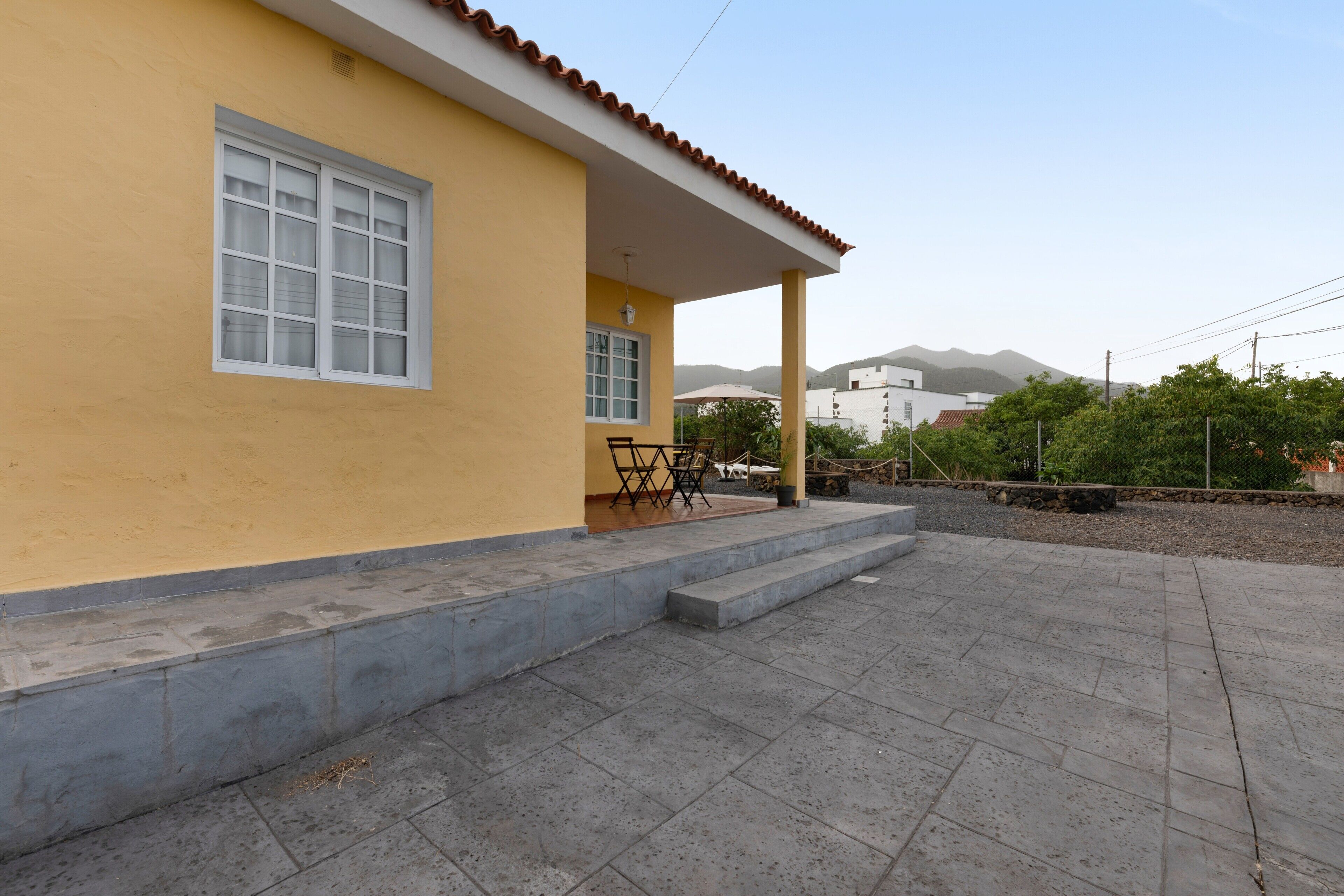 A yellow building with a covered patio, a window, and a chair outside.