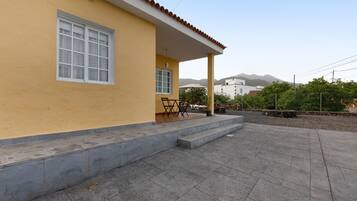 A yellow building with a covered patio, a window, and a chair outside.