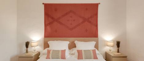 A neatly made bed with two pillows, a bedside table with a lamp, and a wall tapestry.