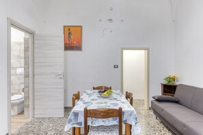 A dining area with a table set for four, a sofa, and a painting on the wall. - Apartment 'Mia' with Shared Terrace and Air Conditioning (Presicce-Acquarica)