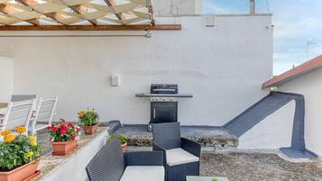 Une terrasse sur le toit, équipée d’un barbecue, de meubles en osier, de plantes en pot et d’un mur blanc.