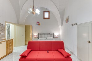 A bedroom with a red sofa, a bed with white linens, a chandelier, and a wooden wardrobe. - Studio Apartment 'Noemi' with Shared Terrace and Air Conditioning (Presicce-Acquarica)