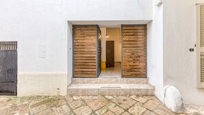 Een gebouwde ingang met een betegeld terras, een houten deur en een stenen muur.