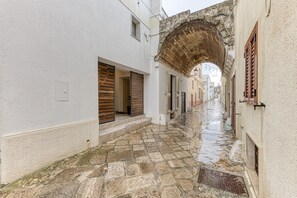 Una estrecha calle adoquinada con edificios blancos, un arco y contraventanas de madera.