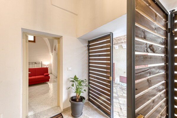 Un pasillo con un sofá rojo, una planta en maceta y una puerta de listones de madera.