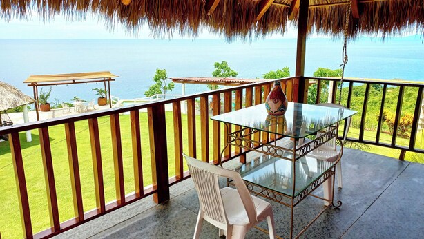 Ein Balkon mit Glastisch und Stühlen mit Blick auf einen Pool und eine malerische Meerlandschaft.