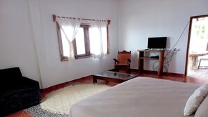Ein Schlafzimmer mit Bett, Sessel, kleinem Tisch, Fernseher und einem Fenster mit Vorhängen.