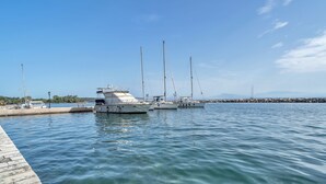 A marina with several sailboats docked, clear water, and a stone pier.