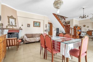 Un espace repas comprenant une table en verre, des chaises à revêtement rouge, un meuble en bois, un canapé, une cheminée et un escalier.