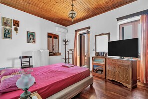 Une chambre avec un plafond en bois, un lit recouvert d’une couverture rose, une commode avec un téléviseur et un radiateur.