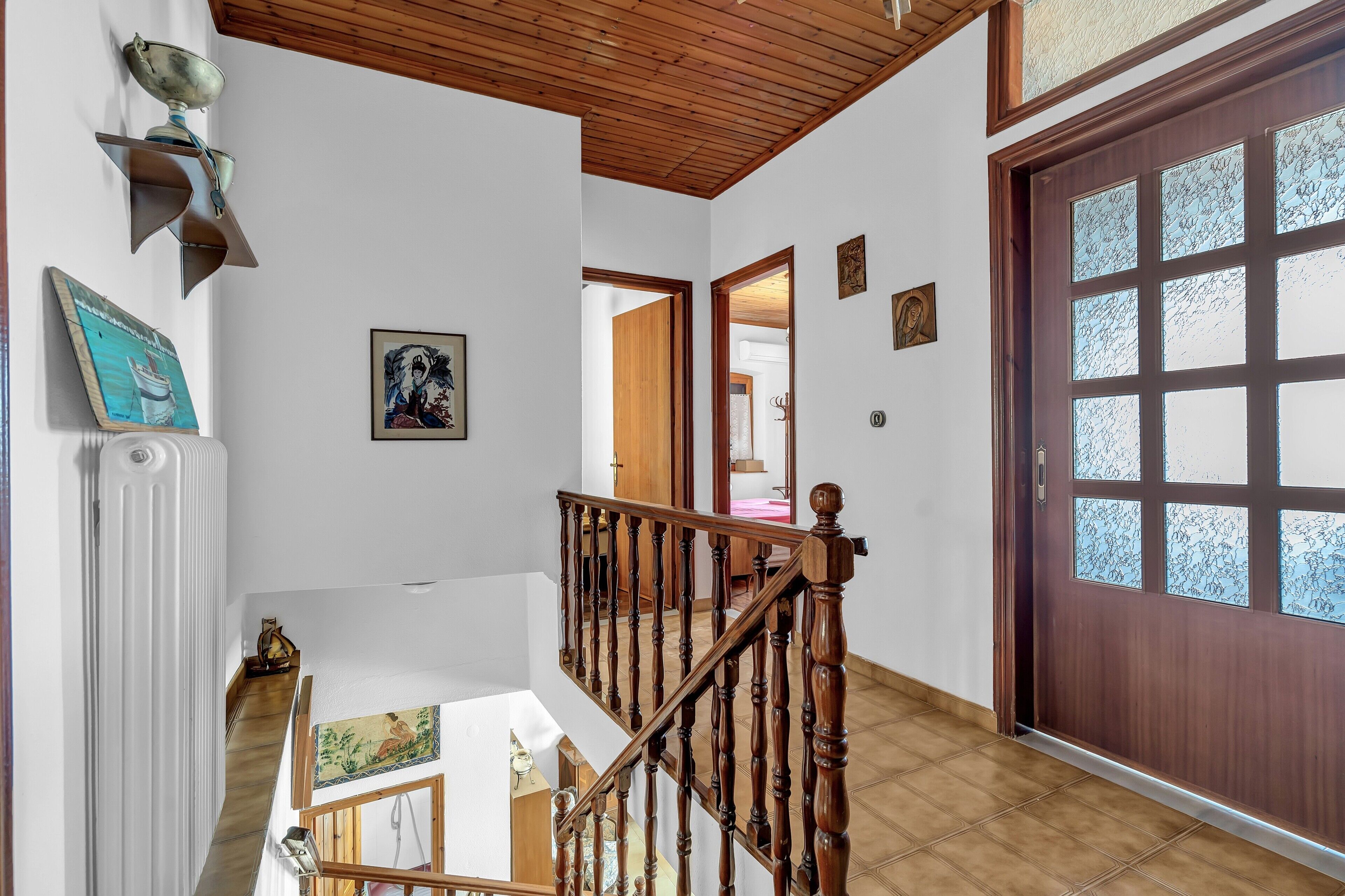 A staircase with wooden railings leading to a second floor, a wooden door with frosted glass panels, and a white radiator on the wall.