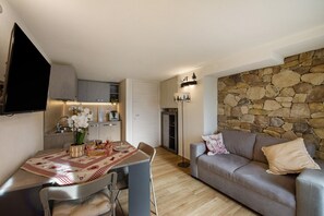 Un espace de vie compact comprenant un coin repas, un canapé, un mur en pierre et une cuisine.
