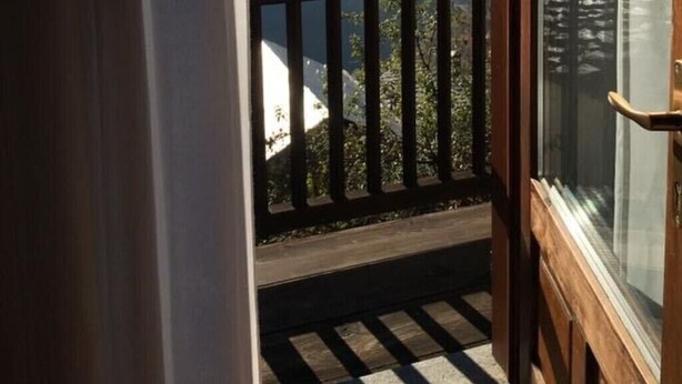 Een balkon met uitzicht op bergen, een houten reling en een raam met gordijn met hertenmotieven.