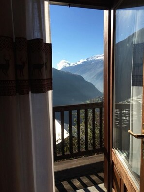 A balcony with a mountain view, a wooden railing, and a window with a curtain featuring deer patterns. - Holiday Home 'Perruchon' with Mountain View, Shared Terrace and Shared Garden (Perloz)