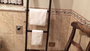 Een badkamer met een houten stoel, een handdoekhouder met twee handdoeken, een raam met gordijn, en een betegelde muur met decoratieve rand.