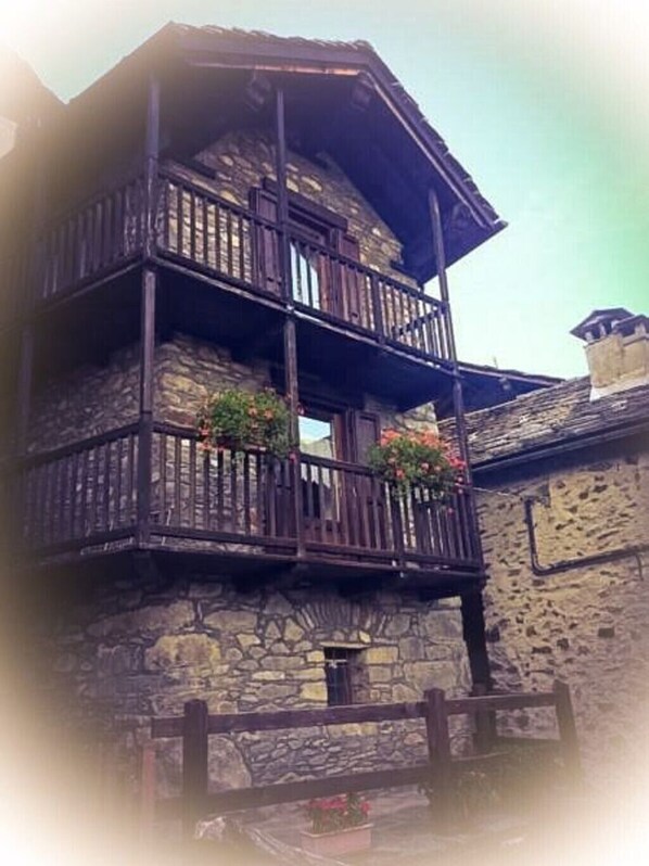 A multi-story stone building with wooden balconies and a stone wall.