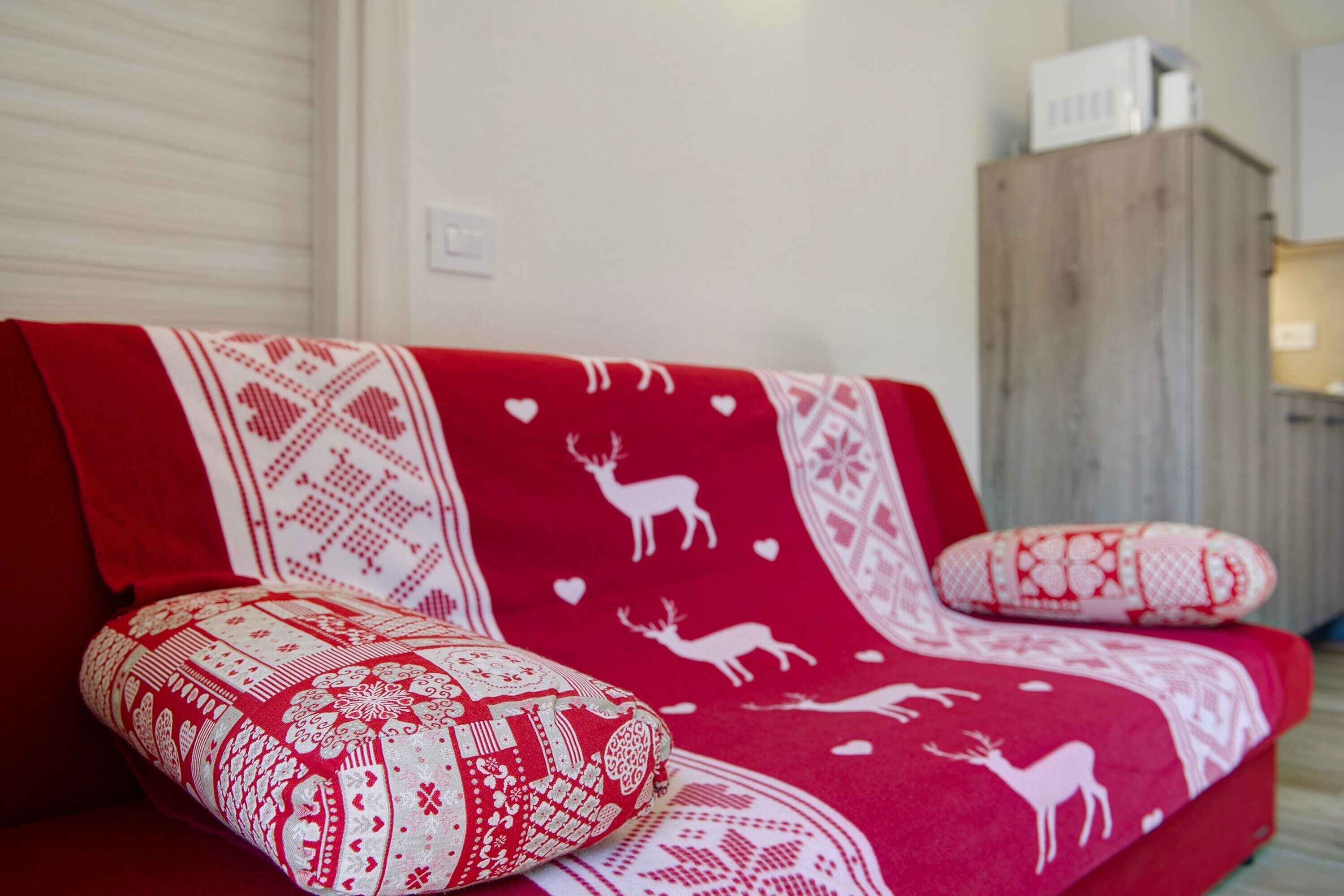 A red sofa with patterned cushions and a blanket with reindeer and hearts.