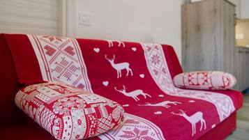 A red sofa with patterned cushions and a blanket with reindeer and hearts.