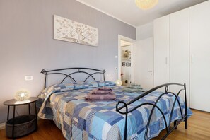 A bedroom with a bed, a bedside table with a lamp, a wall-mounted artwork, and a wardrobe.