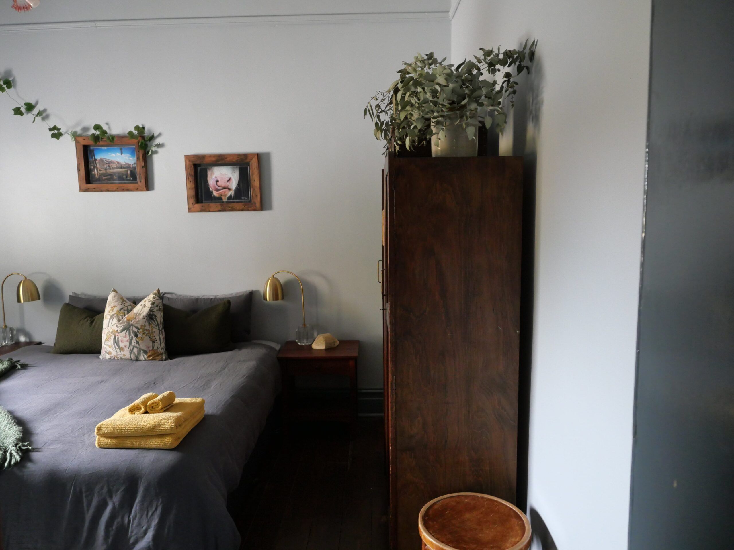 A bedroom with a bed, two bedside tables, a nightstand, a wooden wardrobe, and two wall-mounted pictures.