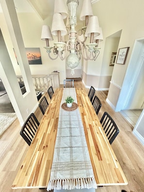 Une salle à manger avec une table en bois, des chaises noires, un tapis au centre et un lustre.