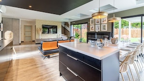 A modern kitchen with a central island, a dining area with chairs, and a living room with a sofa and TV. - Modern Villa with Private Pool (Saint-Aignan-Grandlieu)