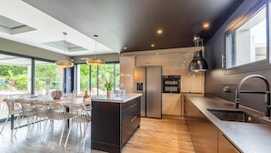 A modern kitchen with a central island, built-in appliances, and a dining area with a large table and chairs. - Modern Villa with Private Pool (Saint-Aignan-Grandlieu)