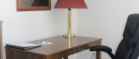 A wooden desk with a red lamp, a black office chair, and a framed picture of a moose on the wall.