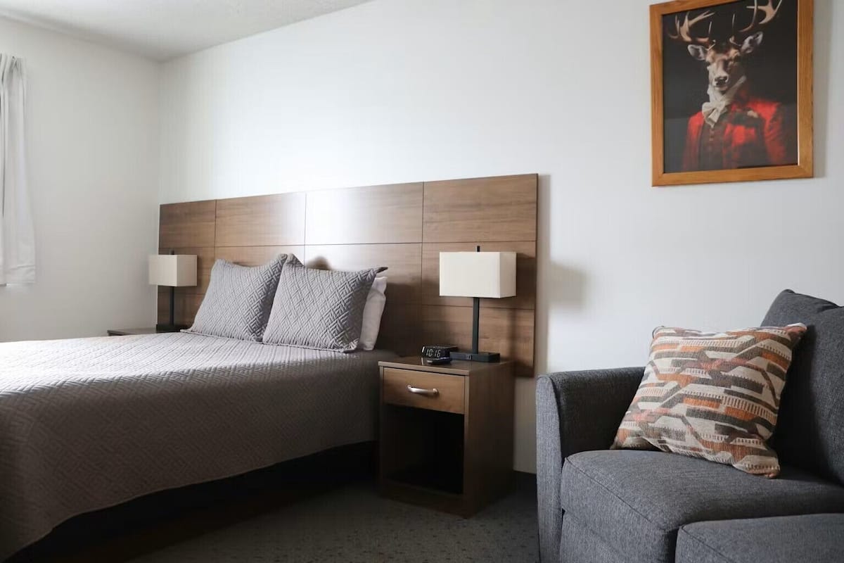Quarto de hotel com uma cama, duas mesas de cabeceira com luminárias, um criado-mudo e um sofá.