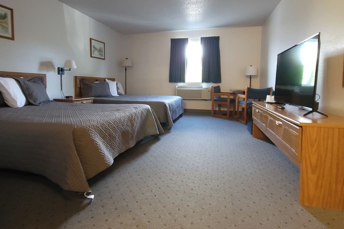 Quarto de hotel com duas camas, uma escrivaninha, uma televisão e uma janela com cortinas.