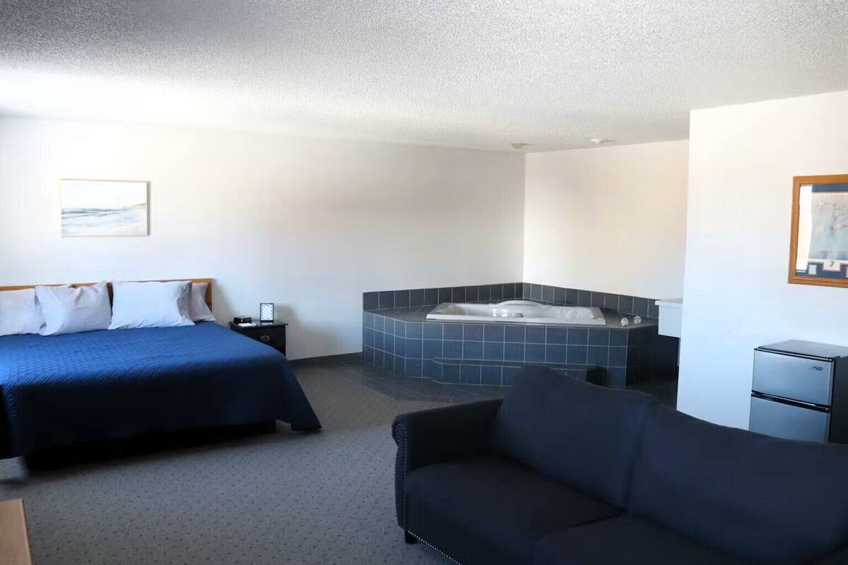 Quarto de hotel com cama, sofá, mesinha, criado-mudo, banheira e frigorífico.