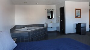 A hotel room with a large bed, a bathtub, a sink, and a refrigerator. - Piper's Inn (Clearbrook)