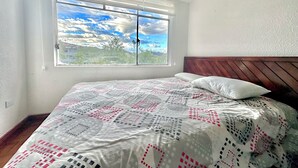 A bedroom with a bed, a window with a view of the sky and clouds, and a wooden headboard.
