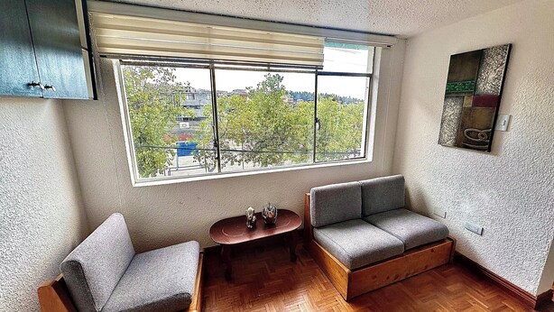 A room with a large window, two grey sofas, a small wooden table, and a wall-mounted artwork.