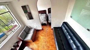 A modern living room with a herringbone wooden floor, a black leather sofa, and grey upholstered chairs.