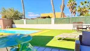 A backyard with a pool, artificial grass, and outdoor furniture.