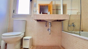 A bathroom with a toilet, sink, shower, and a window.