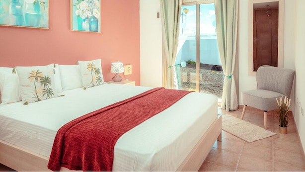 A bedroom with a bed, a chair, a window with curtains, and a painting on the wall.