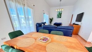A dining area with a wooden table, green upholstered chairs, a bowl of colorful candies, and a blue sofa in the background.