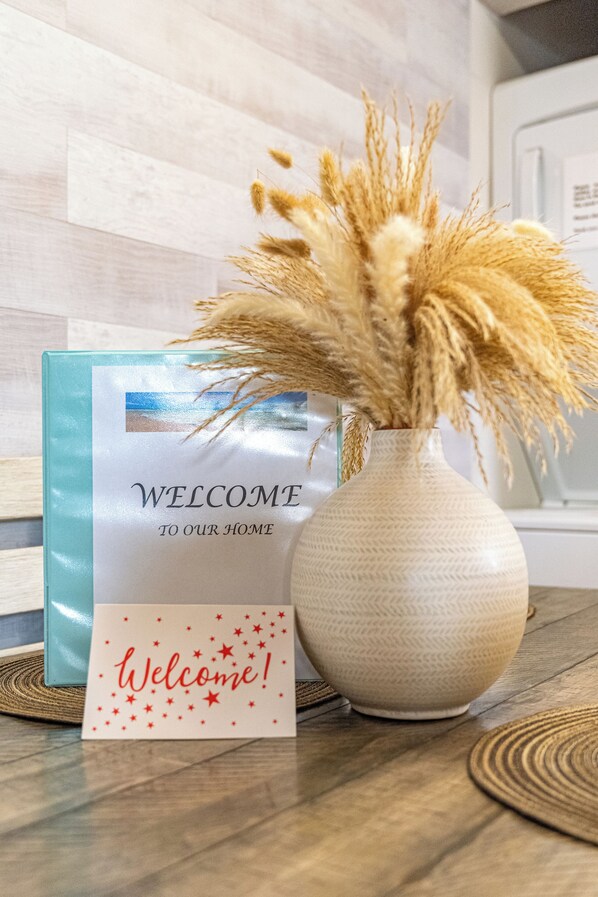 A welcome sign with a beach photo, a vase with dried plants, and a blue card on a wooden floor. - Modern, renovated, centrally located condo with self check in and parking (Ocean City)