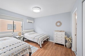 Une chambre avec deux lits, une commode, un élément décoratif mural et une fenêtre avec des stores.