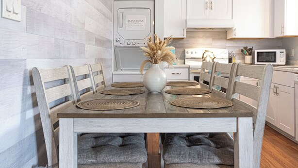 A dining table with four chairs, a vase with dried plants, and a microwave in the background. - Modern, renovated, centrally located condo with self check in and parking (Ocean City)