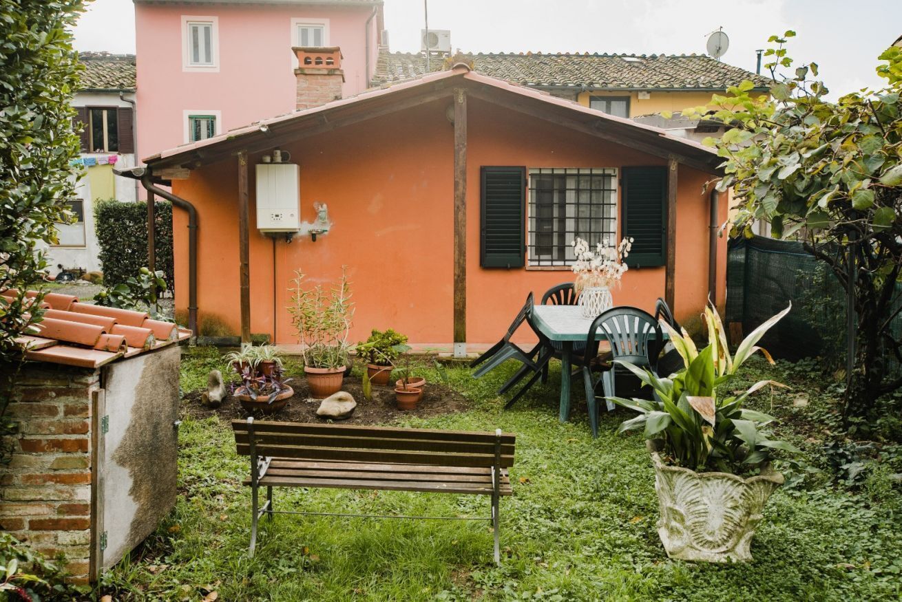 Una piccola casa con giardino, una panchina e un tavolo con sedie.