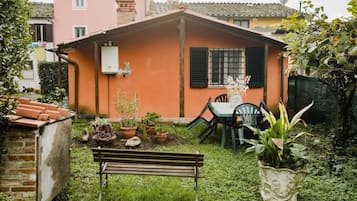 Una piccola casa con giardino, una panchina e un tavolo con sedie.