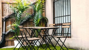 A patio with wooden tables and chairs, surrounded by large potted plants and a wooden fence.