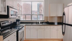 A modern kitchen with white cabinets, a stainless steel refrigerator, a microwave, and a stove.