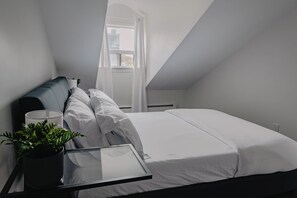 Un dormitorio moderno con una cama, una mesita de noche con una planta y una ventana con cortinas.